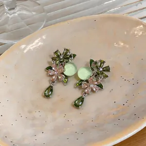 Detailed view of elegant zircon flower earrings with green teardrop pendants on a ceramic dish