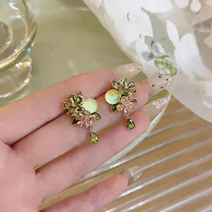 Detailed close-up of elegant green flower drop earrings with zircon crystals held by hand