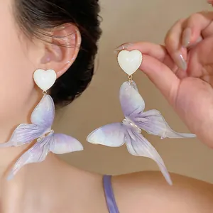 Gros plan d'élégantes boucles d'oreilles papillon en résine violette irisées portées par modèle.