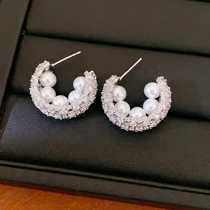 Elegant C-shaped silver stud earrings with white pearls and sparkling zircons on black background