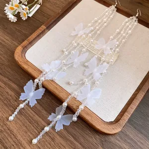 Close-up of white chiffon butterfly and pearl tassel hook earrings displayed on a wooden tray