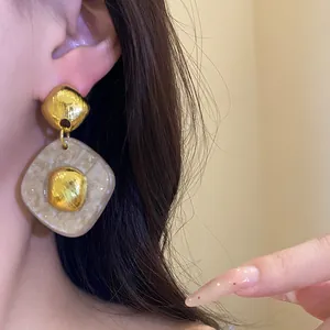 Primo piano di orecchini pendenti vintage in resina a forma di rombo con accenti dorati su modella
