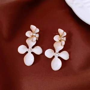 Vue détaillée de boucles d'oreilles pendantes en fleur émaillée blanche avec strass brillants.