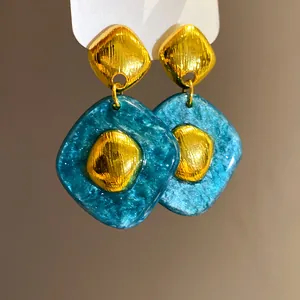 Dettaglio di orecchini vintage in metallo dorato e resina marmorizzata blu ottanio