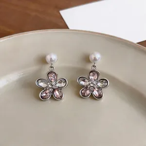 Macro detail of flower earrings with pink crystals and pearls on a beige plate.