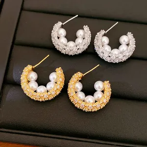 Macro view of C-shaped earrings with pearls and pavé zircons on a leather tray