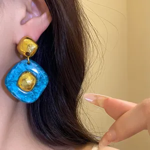 Dettaglio degli orecchini vintage in resina blu a forma di rombo con centri dorati all'orecchio