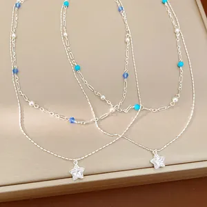 Close-up detail of a double-layered silver necklace with star pendant and blue beads
