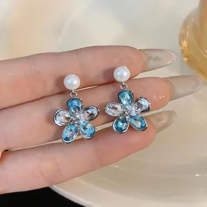 Detailed macro view of elegant flower-shaped pearl earrings with blue gemstones.