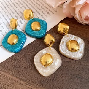 Dettaglio ravvicinato di orecchini vintage in resina blu e crema con accenti dorati