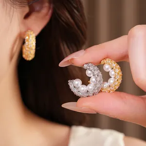 Close-up of C-shaped earrings with pearls and shimmering zircons on model's hand