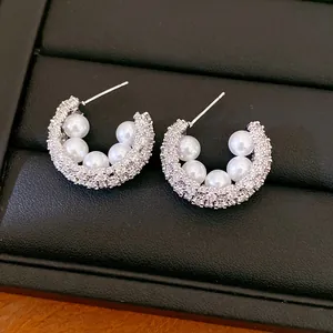 Macro detail of C-shaped silver earrings with sparkling zircons and white pearls