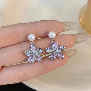 Detail of purple crystal flower earrings with white pearl accents and silver needles