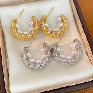 Macro view of C-shaped pearl and cubic zirconia earrings in gold and silver finish