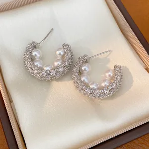 Close-up of elegant C-shaped silver earrings with zircons and pearls in a gift box