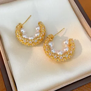 Macro shot of elegant gold-plated C-shaped hoop earrings with pearls and zircon stones