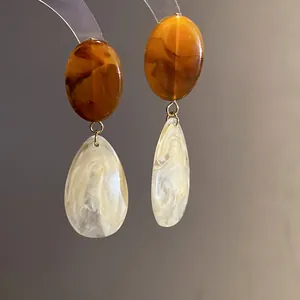Gros plan de boucles d'oreilles en résine avec textures d'ambre et de marbre.