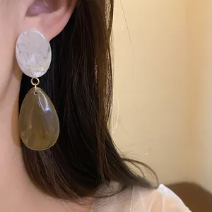 Détail de boucles d'oreilles en résine avec motif marbre blanc et goutte ambre