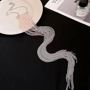 Détail d'un long collier à pompons argentés avec perles roses et fermoir épingle