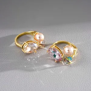 Close-up detail of luxury gold-tone open rings featuring pink pearls and oval crystals.