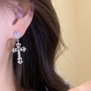 Close-up shot of an ornate 18k gold plated zircon cross drop earring on an ear