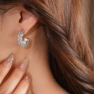 Detailed close-up showing elegant C-shaped zircon and pearl stud earrings on ear