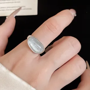 Close-up of minimalist silver plated open ring featuring an iridescent light blue stone
