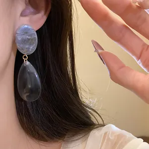 Vue détaillée de boucles d'oreilles pendantes en résine marbrée grise portées par un modèle