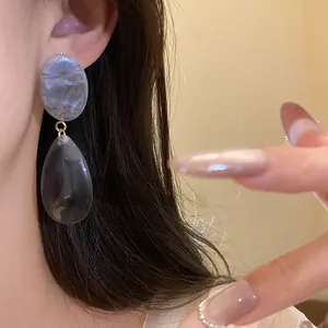 Gros plan détaillé de boucles d'oreilles en résine marbrée grise sur l'oreille du mannequin