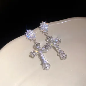 Detailed view of sparkling 18k gold plated zircon cross dangle earrings on a ceramic plate.
