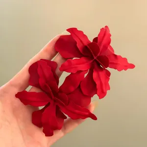 Detail of oversized matte red flower earrings held in hand for vacation style