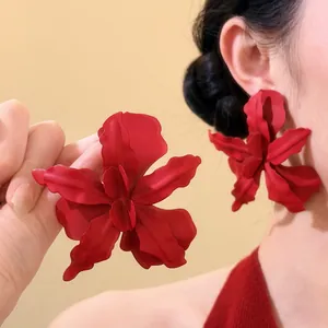 Detailed macro view of oversized matte red floral earrings with 3D petals on a model