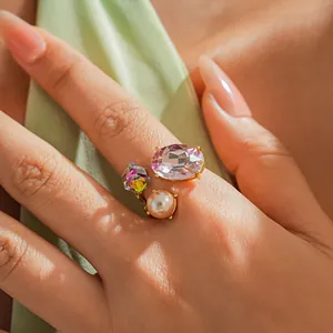 Close-up of elegant gold open ring featuring a purple gem, crystal, and faux pearl