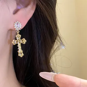 Detailed close-up of elegant gold cross earrings with sparkling zircon stones on a model's ear.