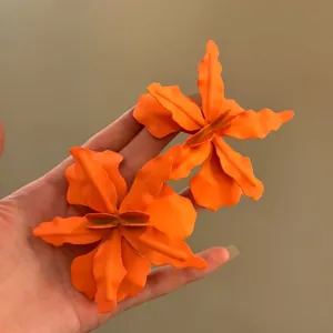 Detail view of large matte orange flower stud earrings for vacation style outfits