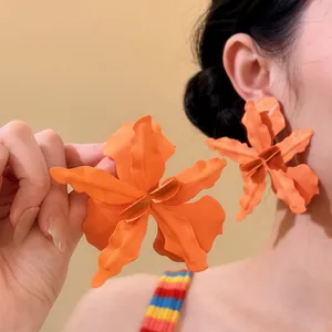 Macro view of oversized matte orange flower earrings on a model for beach vacation