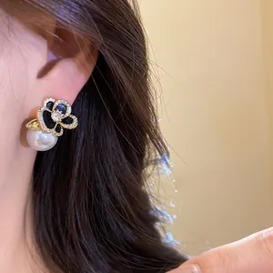 Close-up detail of 14k gold-plated floral stud earrings with zircons and a white pearl drop