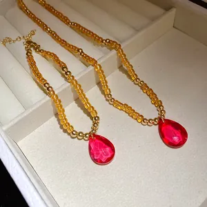 Dettaglio di una collana vintage in ambra con pendente a goccia in vetro rosso vivace.