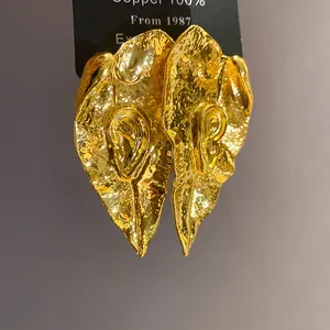 Détail de la texture dorée martelée et du motif d'oreille sur les boucles d'oreilles.