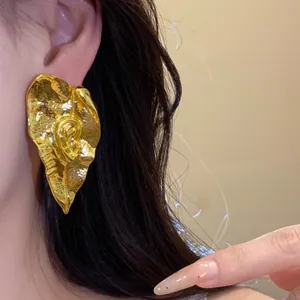 Détail d'une boucle d'oreille vintage en métal doré froissé en forme de feuille.