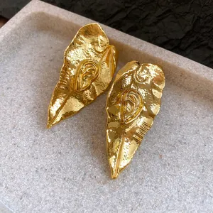 Détail de boucles d'oreilles dorées avec texture de feuille plissée élégante.