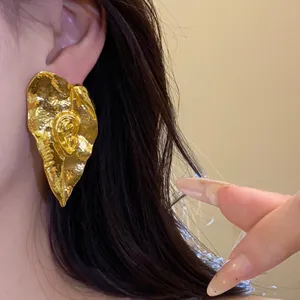 Gros plan sur des boucles d'oreilles dorées en forme de feuille avec relief d'oreille