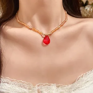 Dettaglio collana di perline vintage con elegante ciondolo a goccia rosso sul collo
