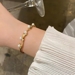 Detailansicht eines eleganten goldenen Wellenarmreifs mit weißen Perlen am Handgelenk