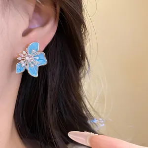 Nahaufnahme blauer Emaille-Blumenohrringe mit Perlen und Zirkonia am Ohr.