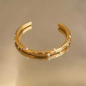 Nahaufnahme eines goldenen Edelstahl-Armreifs mit Perlen und glänzenden Strasssteinen