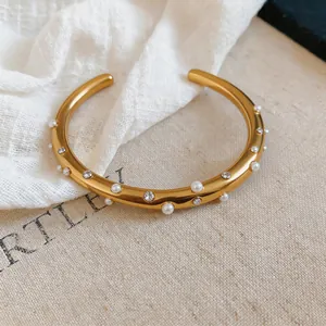 Nahaufnahme eines eleganten goldenen Armreifs aus Edelstahl mit Perlen und Kristallen
