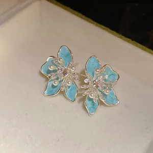Nahaufnahme von hellblauen Emaille-Blumenohrringen mit Zirkonia und Perlen.