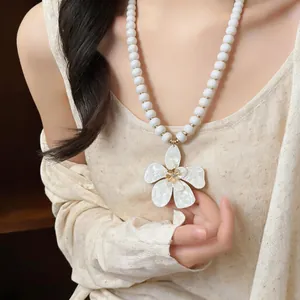 Detailed close-up of a white beaded necklace with a large flower pendant on a model