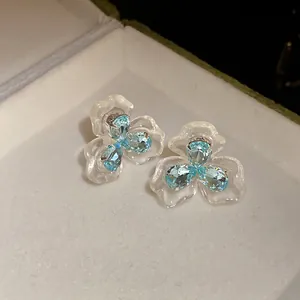 Makroaufnahme eleganter Blumenohrringe mit blauen Zirkoniasteinen und Perlmuttblüten